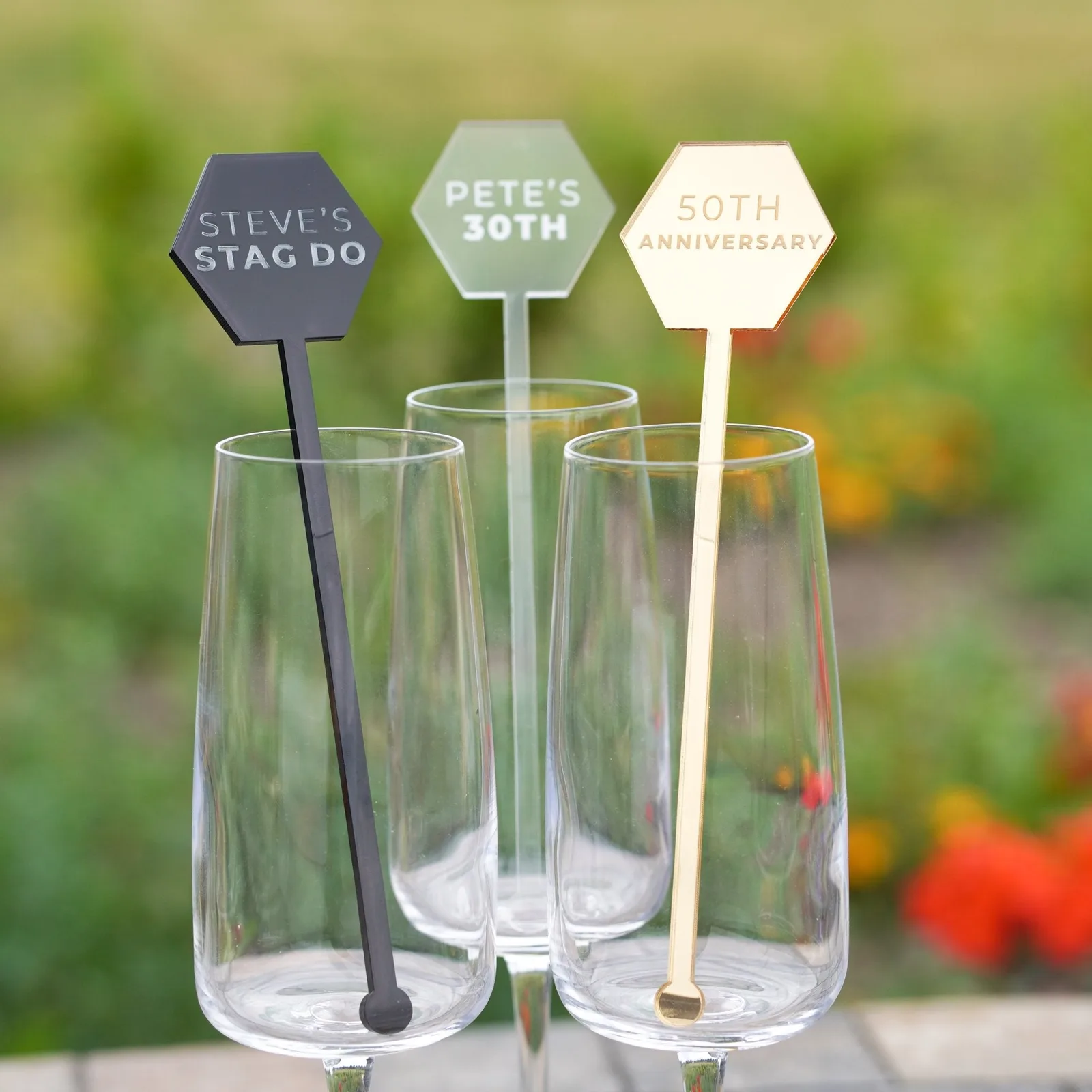 Three hexagon-headed stirrers in black, frosted and mirror gold acrylic, standing in glasses